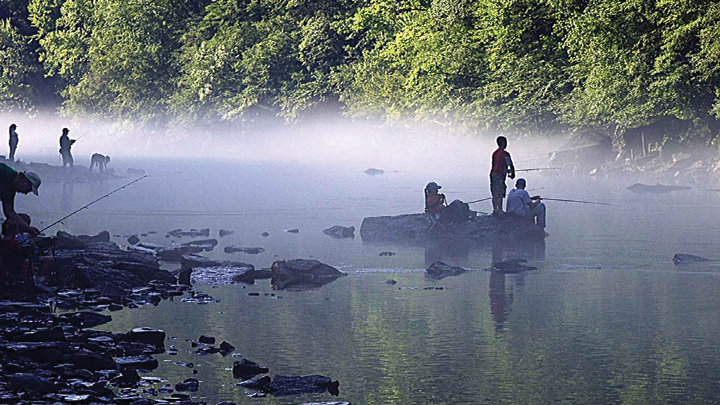 Children fishing on stream in early-morning mist