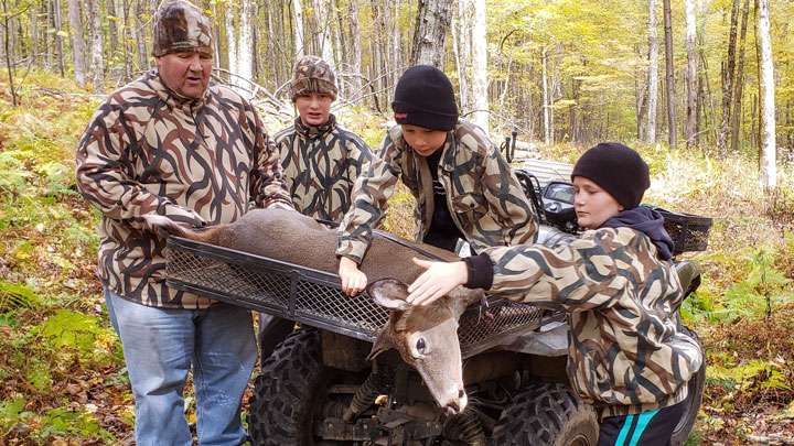 a father and his sons gather around a deer they have hunted