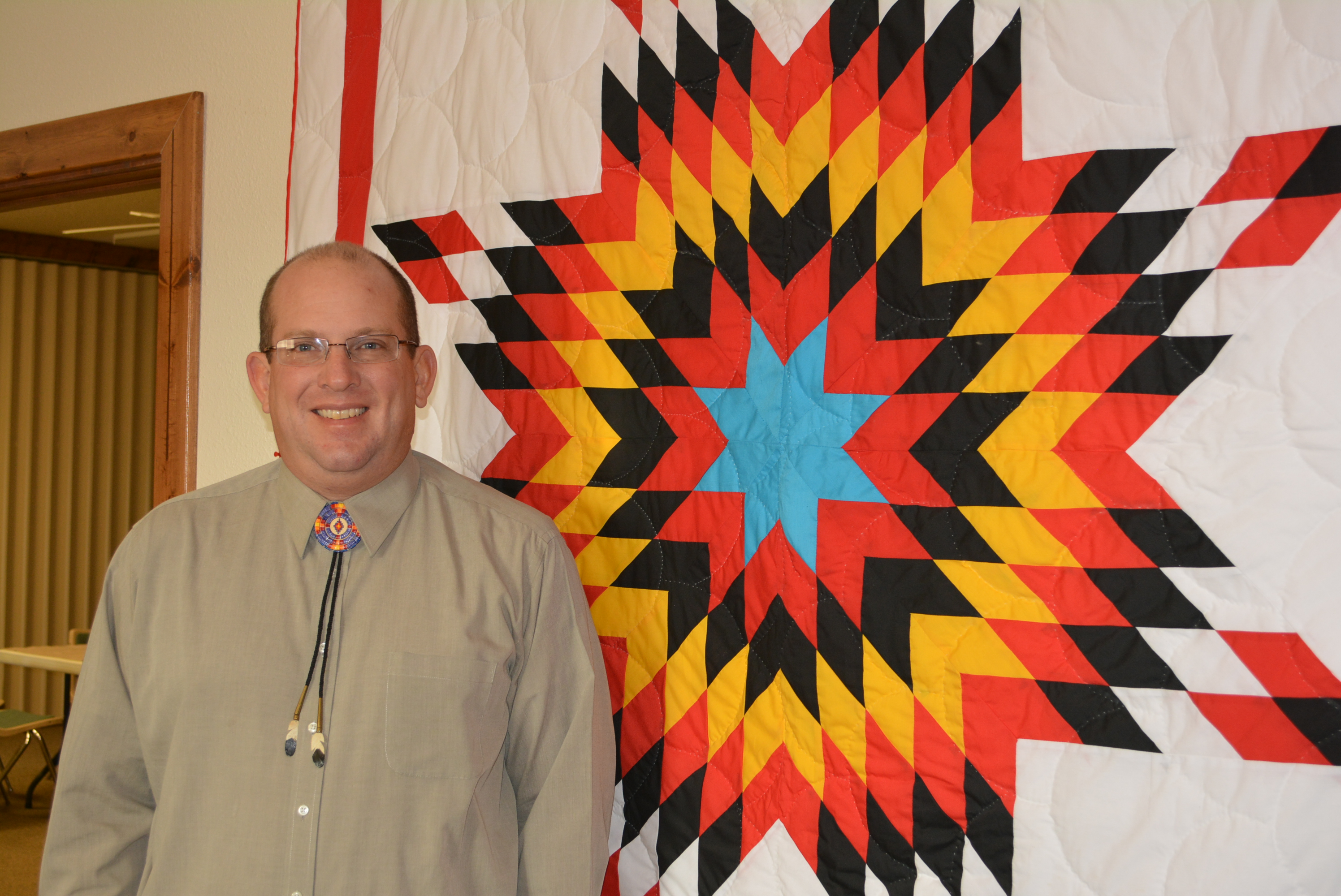 Native American pastor stands before tapestry