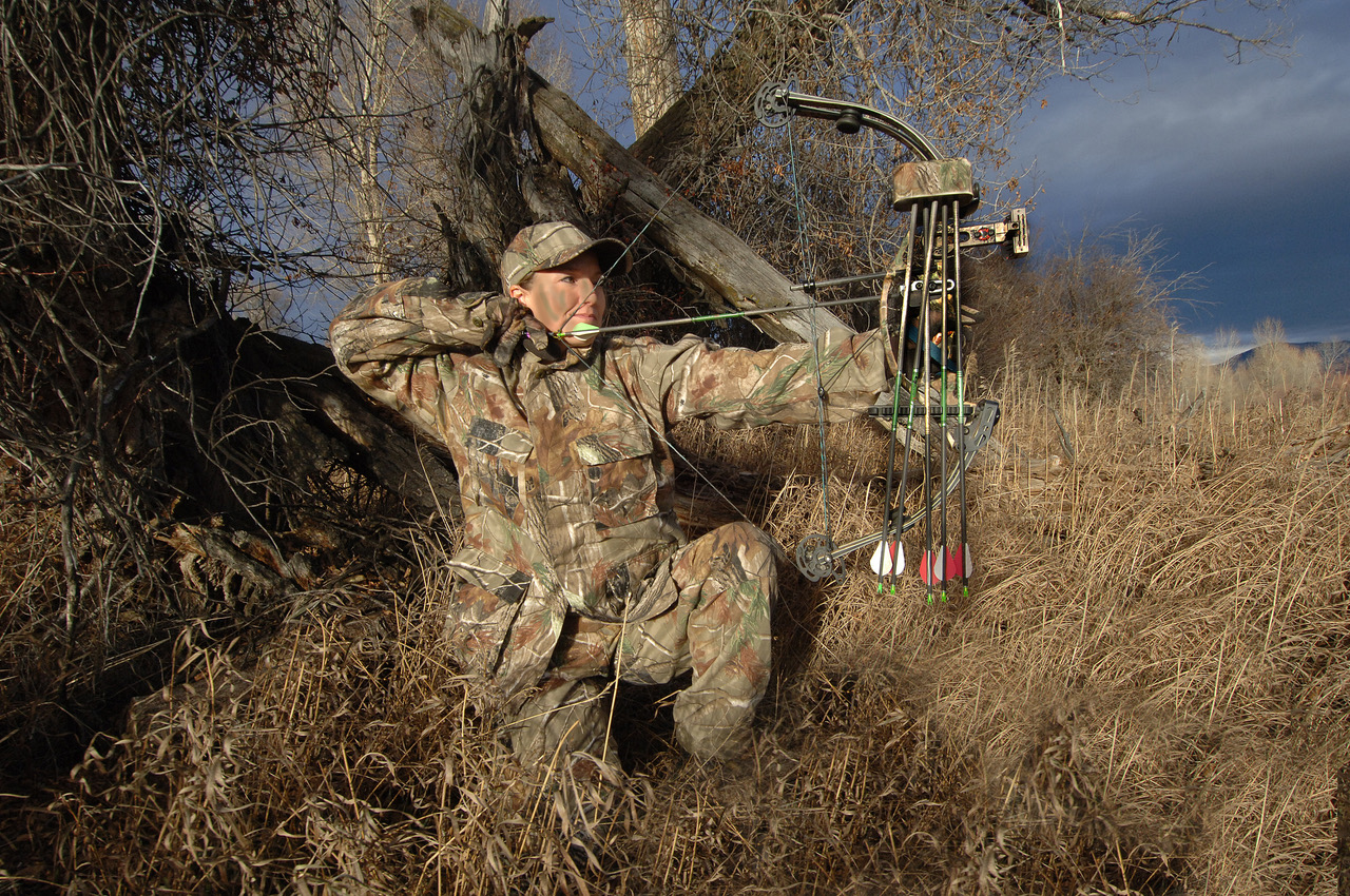 woman bowhunter kneels to take a shot in the field